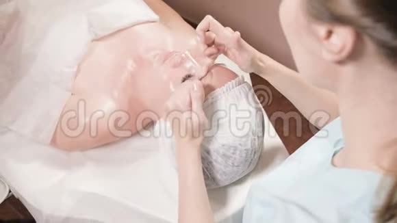 戴着面具和手套的女美容师给一个有魅力的女人做一个有益健康的面部按摩新一代视频的预览图