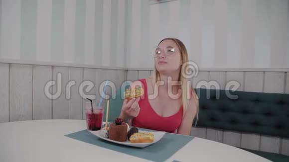 美丽的年轻女孩坐在咖啡馆的一张桌子旁吃着盘子里香甜的新鲜甜点视频的预览图