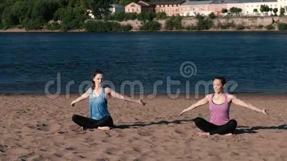 两个女人在城市河边的海滩上伸展瑜伽美丽的城市景色令人讨厌的姿势视频的预览图
