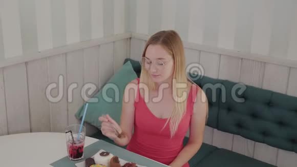 美丽的年轻女孩坐在咖啡馆的一张桌子旁吃着盘子里香甜的新鲜甜点视频的预览图