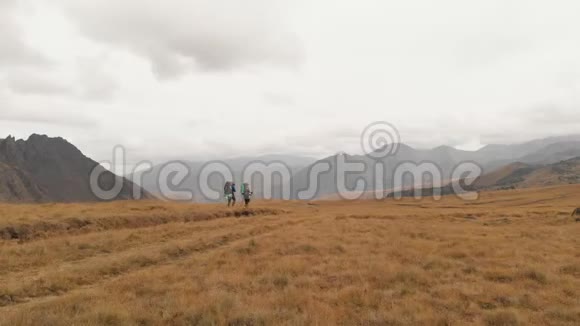 一对戴着帽子和太阳镜的大背包的旅行者男女在高山上漫步的鸟瞰图视频的预览图