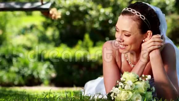 美丽的新娘对着躺在草地上的摄像机微笑视频的预览图