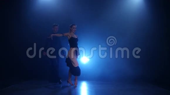 快乐的情侣在烟雾弥漫的工作室里用蓝色聚光灯跳舞拉丁舞视频的预览图