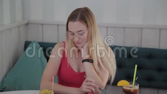 美丽的年轻女孩坐在咖啡馆的一张桌子上有一盘甜点视频的预览图