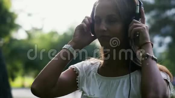 年轻的美女在户外喜欢听耳机音乐视频的预览图