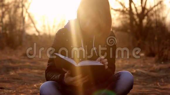 美丽的少女坐在公园里的一片落叶上看书晚霞淡淡概念女孩自由职业者视频的预览图