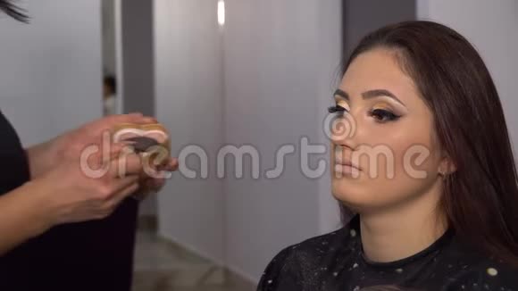 美容院年轻漂亮的女孩模特坐在椅子上化妆师给女孩化妆布鲁奈特的美丽视频的预览图