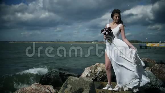 穿着白色连衣裙的漂亮女孩站在海滨手里拿着一束花穿着轻风慢动作视频的预览图