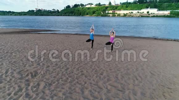 两个女人在城市河边的沙滩上做瑜伽日出时美丽的城市景色视频的预览图