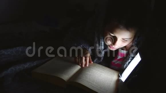一个十几岁的女孩用手电筒躺在毯子下面看书视频的预览图