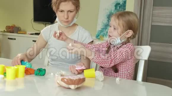 一个年轻的女人和一个女孩用塑料制成牙齿把牙齿插入玩具下巴扮演一个牙医母亲和视频的预览图