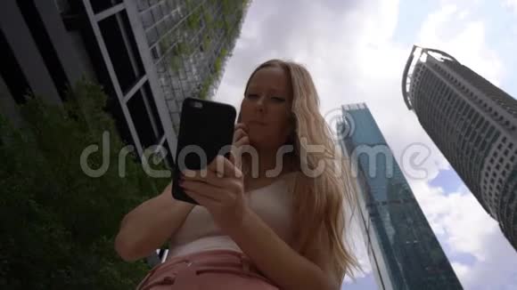 一位年轻女子在市中心使用智能手机背景是摩天大楼视频的预览图