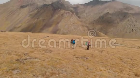 一对戴着帽子和太阳镜的大背包的旅行者男女在高山上漫步的鸟瞰图视频的预览图