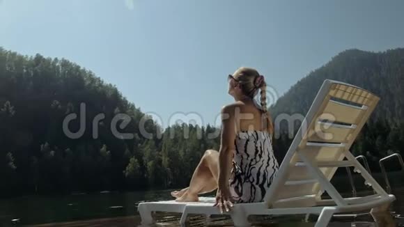 女人躺在日光浴床上戴着太阳镜和一条薄纱披肩女孩在洪水木水下码头休息路面是视频的预览图