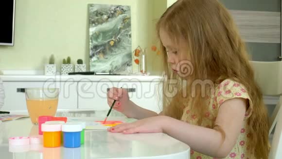 坐在桌旁的一个红发小姑娘画着颜料视频的预览图