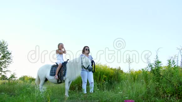 妈妈和女儿在田里走来走去女儿骑着一匹小马妈妈抱着一匹小马做缰绳视频的预览图