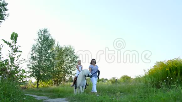 妈妈和女儿在田里走来走去女儿骑着一匹小马妈妈抱着一匹小马做缰绳视频的预览图