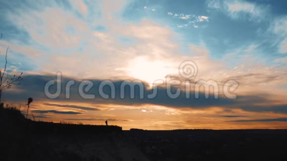 日落时分一个年轻的徒步旅行者女孩背着背包在山顶上的剪影视频的预览图