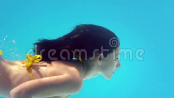 穿着黄色比基尼在水下游泳的美丽的深色头发视频的预览图
