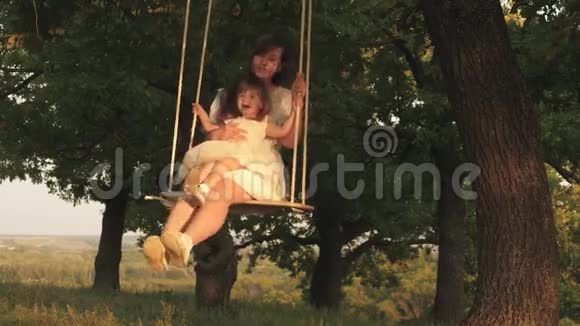 母亲和婴儿在森林中的橡树枝上骑着一条绳秋千妈妈摇着女儿在阳光下摇摆视频的预览图