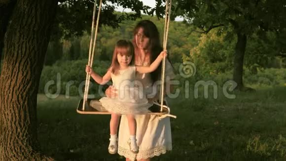 妈妈在阳光下摇动她的女儿母亲和婴儿在森林中的橡树枝上用绳子摆动视频的预览图