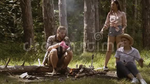 快乐的朋友在大自然中享受篝火一群朋友露营朋友们在炉火上烤着甜棉花糖视频的预览图