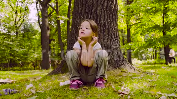一个女孩坐在公园的草地上靠近树视频的预览图