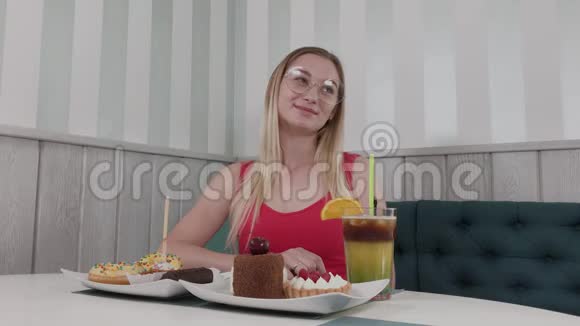 美丽的年轻女孩坐在咖啡馆的一张桌子上有一盘甜点视频的预览图