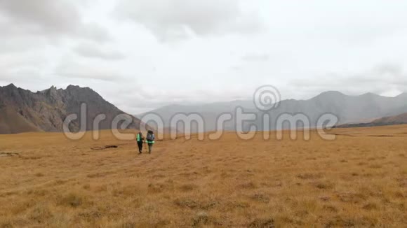 一对戴着帽子和太阳镜的大背包的旅行者男女在高山上漫步的鸟瞰图视频的预览图