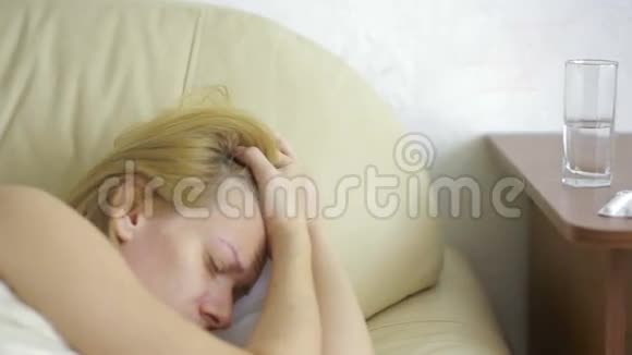 生病的女人躺在床上药丸和一杯水喝药片止痛药视频的预览图