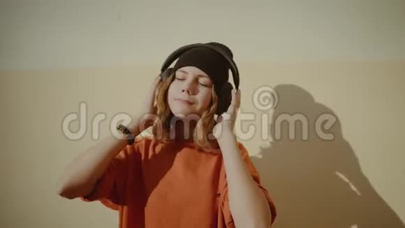 可爱的少女听耳机音乐都市风格时髦的时髦少女戴黑帽听音乐微笑视频的预览图