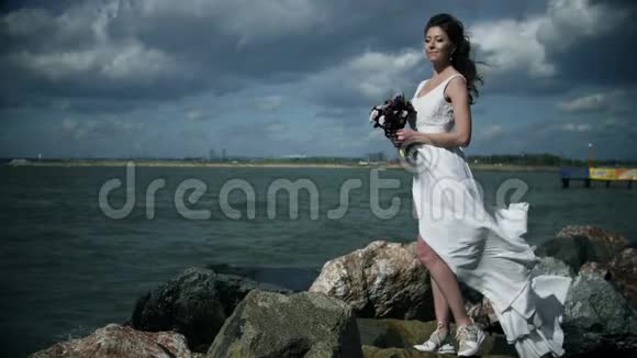 穿着白色连衣裙的漂亮女孩站在海滨手里拿着一束花穿着轻风慢舞视频的预览图