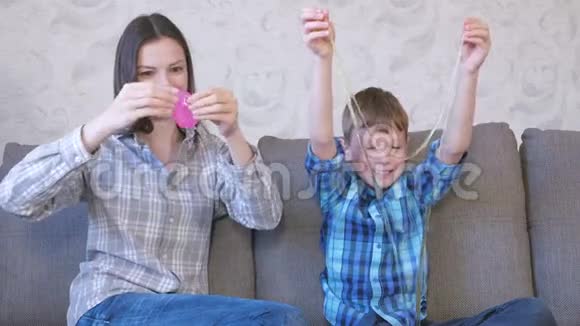 快乐的妈妈和儿子坐在沙发上玩黏液视频的预览图
