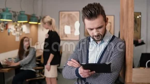 年轻英俊的胡子男在现代创业办公室使用触摸屏平板电脑视频的预览图