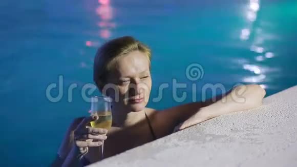 晚上的女人在泳池里喝着热水喝着一杯香槟视频的预览图
