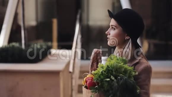 穿着时尚外套的年轻美女拿着一包产品走在街上微笑着视频的预览图