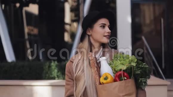 年轻漂亮的女人穿着时髦的外套走在街上手里拿着一包产品微笑着看着视频的预览图