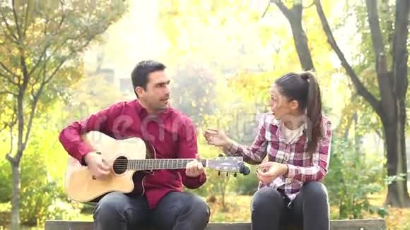 男人一边弹吉他一边和女人一起唱歌一边坐在公园的长椅上视频的预览图