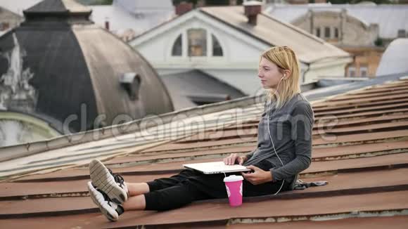 年轻女子坐在屋顶上手提电脑和耳机听音乐视频的预览图