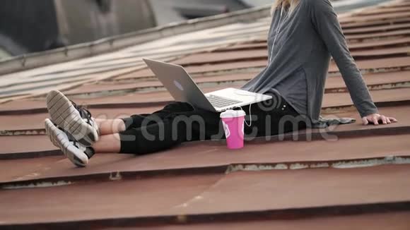 年轻女子坐在屋顶上手提电脑和耳机听音乐视频的预览图