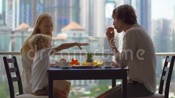 年轻的一家人在摩天大楼的阳台上吃早餐午餐可以看到整个市中心视频的预览图