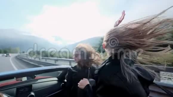 两个美丽的年轻女孩坐在山间的红色小屋里公路上的路穿着黑色皮革视频的预览图
