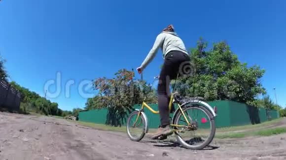 在一个村庄的乡村道路上骑着老式自行车的年轻妇女视频的预览图