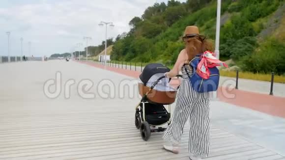 快乐的年轻母亲带着婴儿车在长廊散步家庭母性和人的概念有婴儿的幸福母亲视频的预览图