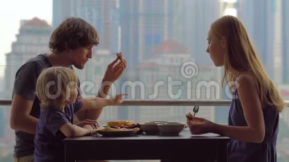 年轻的一家人在摩天大楼的阳台上吃早餐午餐可以看到整个市中心视频的预览图