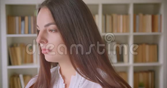 一位年轻的白种人女学生用书架在图书馆的室内看着摄像机的特写照片视频的预览图