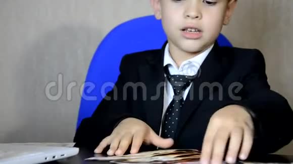 年轻的商人用笔记本电脑现代办公室时尚儿童帅哥坐在扶手椅的桌子旁数着钱视频的预览图