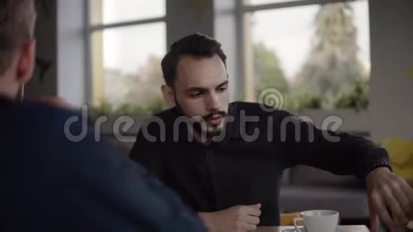 两个开朗的商人正在讨论什么一边微笑着坐在咖啡馆里拿着笔记本电脑和电话二视频的预览图