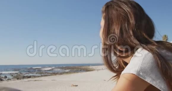 坐在沙滩上微笑的年轻女子视频的预览图