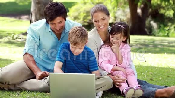 一家人拿着笔记本电脑坐在草地上微笑视频的预览图